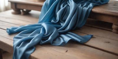 The primary subject of the image is a blue scarf, which is draped over a wooden table. The setting is a wooden table, and the visual style appears to be a photo. The dominant colors in the image are blue and white, creating a calm and serene atmosphere.