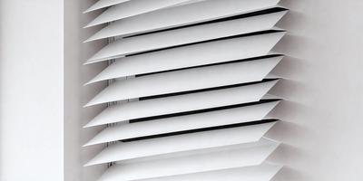The primary subject of the image is a white shade or blind on a window. The setting is indoors, with the window being the main focus of the image. The visual style appears to be a photo, capturing the details of the shade or blind. The colors in the image are predominantly white, giving the scene a clean and minimalist appearance.