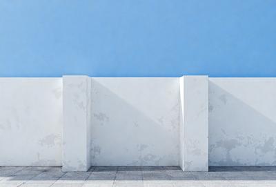 The primary subject of the image is a white wall with a blue sky in the background. The wall appears to be a part of a building, and it is situated next to a concrete wall. The visual style of the image is a photo, capturing the natural light and colors of the scene. The colors and mood of the image are predominantly blue and calm, creating a serene atmosphere.