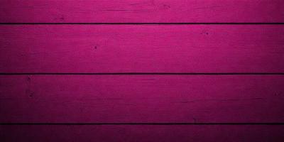 The primary subject of the image is a wooden wall with a pinkish hue. The setting is a room with a wooden floor. The visual style is a close-up of the wooden wall, showcasing its texture and color. The dominant colors are pink and brown, creating a warm and inviting atmosphere.