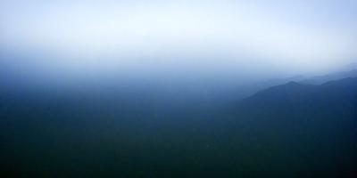 The primary subject of the image is a mountain range, with a blue sky serving as the backdrop. The visual style appears to be a photo, capturing the natural beauty of the landscape. The colors and mood of the image are predominantly blue, creating a serene and peaceful atmosphere.