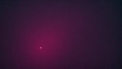 The primary subject of the image is a red sun, which is the main object in the scene. The setting is a dark, pink background, which creates a moody atmosphere. The visual style is a photo, capturing the sun's rays and the pink sky. The colors and mood of the image are dominated by the red sun and the pink background, creating a striking and dramatic scene.