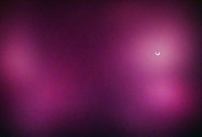 The primary subject of the image is a crescent moon, which is the main object in the scene. The setting is a purple background, which creates a unique and visually striking environment. The visual style of the image is a photo, capturing the moon in its natural setting. The colors and mood of the image are predominantly purple, giving it a calm and serene atmosphere.