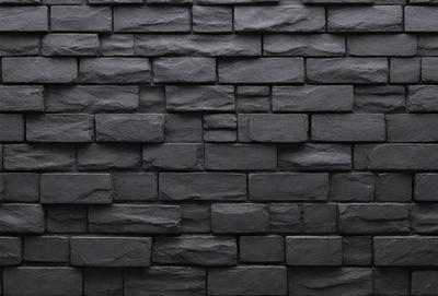 The primary subject of the image is a large black brick wall. The setting is a dark room, and the visual style is a close-up of the brick wall. The dominant colors are black, and the overall atmosphere is dark and moody.