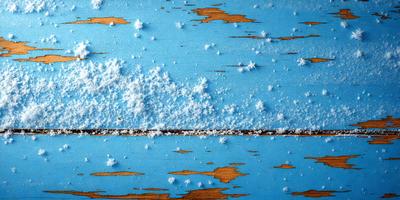 The primary subject of the image is a blue wooden table with a white substance, possibly snow or frost, covering its surface. The setting is an outdoor environment, with the table being the main focus of the scene. The visual style of the image is a photo, capturing the white substance on the wooden table. The colors and mood of the image are predominantly white and blue, creating a serene and cold atmosphere.