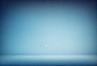 The primary subject of the image is a blue sky with a few white stars visible. The setting is a vast, open space with no visible landmarks or objects. The visual style is a black and white photo, which adds a sense of timelessness and simplicity to the scene. The colors and mood convey a sense of tranquility and vastness, as the viewer is left to appreciate the beauty of the star-filled sky.