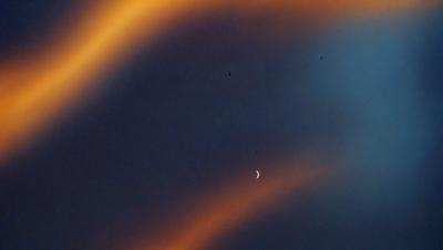 The primary subject of the image is a moon, which is the main object in the scene. The setting is a dark, cloudy sky, with the moon being the only bright spot in the background. The visual style of the image is a photo, capturing the moon and its surroundings. The colors in the image are predominantly dark, with the moon being the only light source, creating a moody atmosphere.