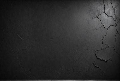 The primary subject of the image is a black wall with a cracked texture. The setting is a dark room, and the visual style is a close-up of the wall. The colors and mood of the image are predominantly dark and moody, with the cracked texture adding an element of distress or decay.