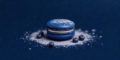 The primary subject of the image is a blue macaroon with a yellow filling, sitting on a blue surface. The setting is a table with a blue background. The visual style is a photo, and the colors and mood are predominantly blue, creating a calm and soothing atmosphere.
