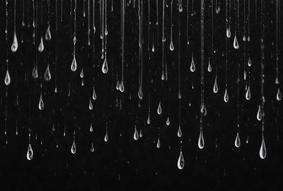 The primary subject of the image is a rainy scene with a black background. The setting is a rainy day, and the visual style is a photo. The image features a large number of raindrops falling from the sky, creating a moody and atmospheric scene. The dominant colors are black and white, with the raindrops being the main focus of the image.
