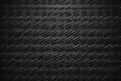The primary subject of the image is a close-up of a black metal surface, possibly a grate or a piece of armor. The setting is a dark room, and the visual style appears to be a photo. The dominant colors are black and grey, creating a moody atmosphere.