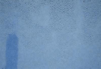The primary subject of the image is a blue wall with a textured surface. The setting is a room with a blue wall, and the visual style is a close-up of the wall. The dominant colors are blue and white, creating a calm and serene atmosphere.