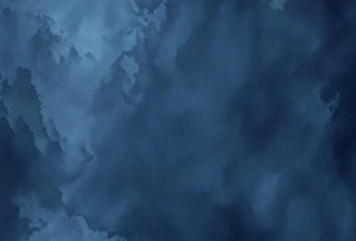 The primary subject of the image is a cloudy blue sky. The setting is a vast expanse of the sky, with no visible land or other objects. The visual style is a natural, outdoor scene. The colors and mood are predominantly blue, with a slightly moody atmosphere.