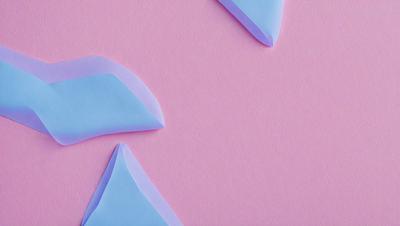 The primary subject of the image is a pink background with three blue triangles cut out of it. The triangles are placed in different positions on the pink surface, creating a visually interesting and unique design. The setting appears to be a creative or artistic environment, as the triangles are cut out of the pink paper, giving the impression of a craft or art project. The visual style of the image is a combination of digital art and illustration, as the triangles are carefully cut and placed on the pink surface