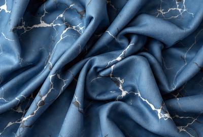 The primary subject of the image is a blue fabric with a marbled pattern. The setting is a close-up of the fabric, showcasing its intricate design. The visual style is a detailed, up-close view of the fabric, emphasizing its texture and pattern. The colors and mood of the image are predominantly blue, creating a calm and serene atmosphere.