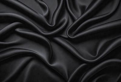 The primary subject of the image is a close-up of a black fabric, possibly a piece of clothing or a curtain. The setting is a dark background, which emphasizes the fabric's texture and pattern. The visual style appears to be a photo, as it captures the details of the fabric. The colors and mood of the image are predominantly dark, with the black fabric being the main focus.