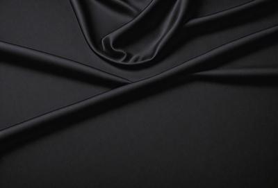 The primary subject of the image is a black fabric, possibly a piece of silk, with a pattern of white stripes. The setting is a dark background, which contrasts with the fabric. The visual style appears to be a close-up of the fabric, showcasing its texture and pattern. The colors and mood of the image are predominantly dark, with the white stripes on the black fabric providing a subtle contrast.