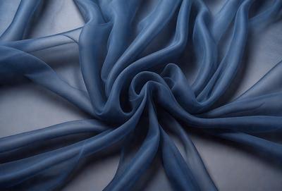 The primary subject of the image is a blue fabric, possibly a piece of cloth or a curtain, with a swirling pattern. The setting is a white surface, which provides a clean and uncluttered backdrop for the fabric. The visual style of the image is a combination of photo and digital art, as it appears to be a close-up of the fabric with a slightly blurred background. The dominant colors in the image are blue and white, creating a calm and serene atmosphere.