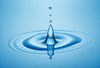 The primary subject of the image is a single drop of water, which is captured in mid-air. The setting is a blue background, which adds to the overall visual style. The image is a photo, showcasing the natural beauty of the water drop. The colors are predominantly blue, creating a calm and serene atmosphere.