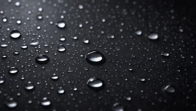 The primary subject of the image is a close-up of a black surface with water droplets on it. The setting is a dark background, and the visual style appears to be a photo. The colors in the image are predominantly black and white, with the water droplets adding a touch of gray. The overall atmosphere is moist and somewhat mysterious.