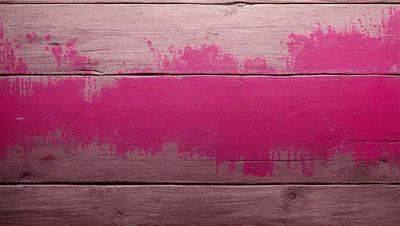 The primary subject of the image is a pink paint splatter on a wooden surface. The setting is a wooden wall, and the visual style appears to be a photo. The dominant colors are pink and brown, creating a warm and vibrant atmosphere.