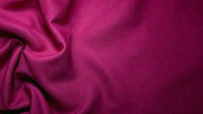The primary subject of the image is a piece of pink fabric. The setting is a room with a pink background. The visual style is a close-up of the fabric, showcasing its texture and color. The dominant colors are pink, and the overall atmosphere is soft and warm.