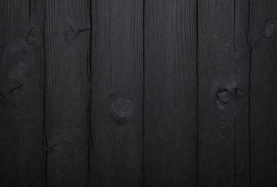 The primary subject of the image is a wooden wall with a black surface. The setting is a room with a black wall, and the visual style is a close-up of the wooden wall. The colors and mood of the image are predominantly dark, creating a moody atmosphere.