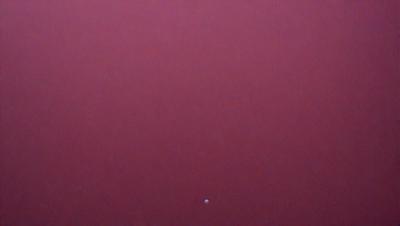 The primary subject of the image is a red background, which appears to be a wall or a surface. The setting/background is a dark, possibly purple, color that contrasts with the red. The visual style of the image is a close-up of the red background, which gives a sense of depth and texture. The colors and mood of the image are bold and striking, with the red and purple hues creating a dramatic and intense atmosphere.