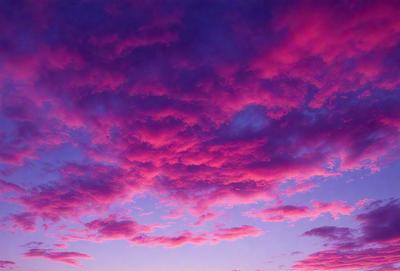 The primary subject of the image is a beautiful pink sky with clouds. The setting is a cloudy sky, and the visual style is a photo. The dominant colors are pink and purple, creating a serene and calming atmosphere.