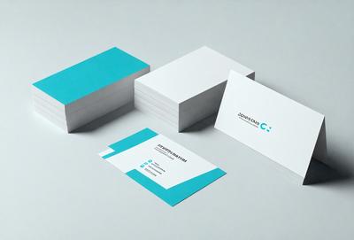 The primary subject of the image is a stack of business cards. The cards are white with blue accents, and they are arranged in a neat pile. The setting is a table, and the visual style is a close-up of the cards. The colors and mood of the image are predominantly white and blue, giving it a clean and professional appearance.