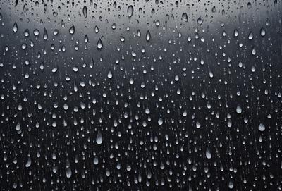 The primary subject of the image is a rainy day, as evidenced by the raindrops falling on the ground. The setting is an outdoor environment, with the raindrops falling on a black background. The visual style is a photo, capturing the raindrops in their natural form. The colors and mood of the image are predominantly dark and moody, with the raindrops creating a sense of wetness and gloominess.