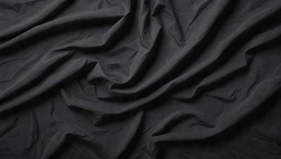The primary subject of the image is a black fabric, which appears to be a piece of cloth or a curtain. The setting is a dark background, which contrasts with the black fabric. The visual style is a close-up of the fabric, showcasing its texture and details. The colors and mood of the image are predominantly dark, with the black fabric being the main focus.