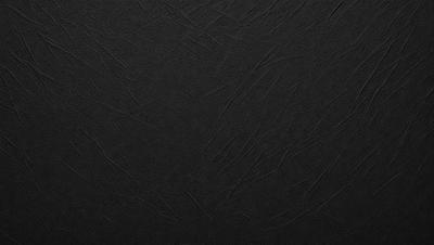 The primary subject of the image is a black leather surface. The setting is a black background, which creates a striking contrast with the leather. The visual style is a close-up of the leather, showcasing its texture and details. The colors and mood of the image are predominantly dark, with the black leather and background creating a moody and dramatic atmosphere.
