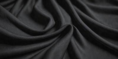 The primary subject of the image is a black fabric, which appears to be a piece of cloth or a curtain. The setting is a dark background, which contrasts with the black fabric. The visual style is a close-up of the fabric, showcasing its texture and details. The colors and mood of the image are predominantly dark, with the black fabric being the main focus.