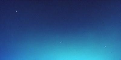 The primary subject of the image is the moon, which is seen in the sky against a backdrop of a blue, cloudless sky. The visual style of the image is a photo, capturing the beauty of the moon and the vastness of the sky. The colors and mood of the image are predominantly blue, creating a serene and peaceful atmosphere.