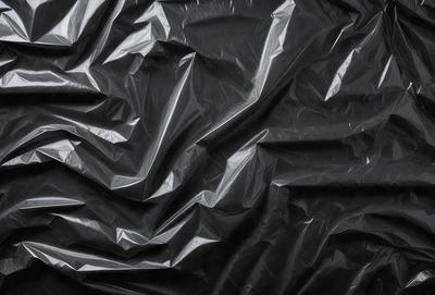 The primary subject of the image is a close-up of a black plastic bag. The setting is a dark background, which emphasizes the plastic bag. The visual style is a black and white photo, giving the image a classic and timeless appearance. The colors and mood are predominantly dark, with the plastic bag being the main focus of the image.