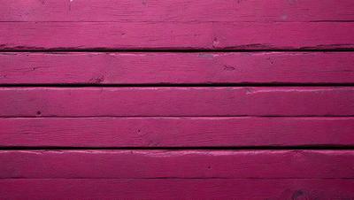 The primary subject of the image is a wooden wall painted in a deep shade of pink. The setting is a room with a wooden floor, and the visual style is a close-up of the wall. The colors and mood of the image are predominantly pink, creating a warm and inviting atmosphere.