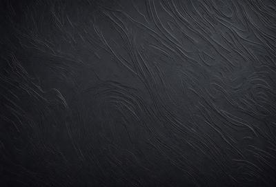The primary subject of the image is a black background with a pattern of swirls and waves. The setting is a dark room, and the visual style appears to be a combination of a photo and a digital art or illustration. The dominant colors are black and grey, creating a moody and dramatic atmosphere.