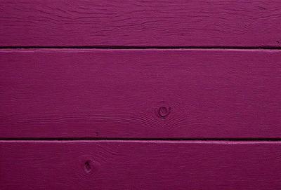 The primary subject of the image is a wooden wall with a purple color. The setting is a room with a wooden surface, and the visual style is a close-up of the wooden wall. The dominant colors are purple and brown, creating a warm and cozy atmosphere.