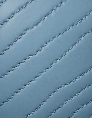 The primary subject of the image is a blue leather material with a pattern of zigzag stitching. The setting is a close-up of the leather material, showcasing the intricate design of the stitching. The visual style is a detailed, up-close view of the leather material, highlighting its texture and craftsmanship. The colors and mood of the image are predominantly blue, giving it a calm and sophisticated atmosphere.