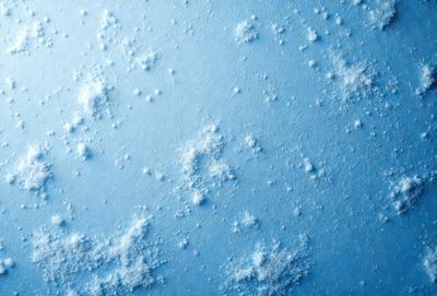 The primary subject of the image is a blue background with white snowflakes scattered across it. The setting appears to be a winter scene, possibly a painting or digital artwork. The visual style gives the impression of a textured, snowy surface. The dominant colors are blue and white, creating a calm and serene atmosphere.