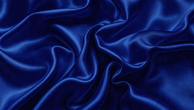 The primary subject of the image is a blue fabric, which appears to be a piece of silk. The setting is a close-up of the fabric, showcasing its texture and details. The visual style is a realistic representation of the fabric, with no indication of it being a photo, digital art, illustration, drawing, pattern, texture, or clipart. The dominant colors are blue and purple, creating a calm and serene atmosphere.