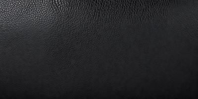 The primary subject of the image is a black leather material. The setting is a black background, which creates a contrast with the leather material. The visual style is a close-up of the leather material, showcasing its texture and details. The colors and mood of the image are predominantly dark, with the black leather material being the main focus.