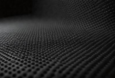 The primary subject of the image is a close-up of a black mesh material, possibly a net or a patterned surface. The setting is a dark room, and the visual style appears to be a photo. The dominant colors are black and white, creating a moody atmosphere.