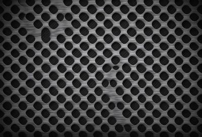The primary subject of the image is a pattern of small circles, which are arranged in a grid-like formation. The setting is a black background, which contrasts with the circles, making them stand out. The visual style is a close-up of the pattern, showcasing the intricate details of the circles. The colors and mood of the image are predominantly black and white, giving it a clean and minimalist appearance.