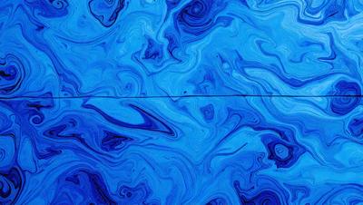 The primary subject of the image is a blue, swirling, and patterned surface, which appears to be a piece of art or a decorative item. The setting is a blue background, and the visual style is a combination of artistic and digital elements. The dominant colors are blue and white, creating a calming and visually appealing atmosphere.