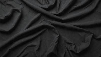 The primary subject of the image is a black fabric, which is the main object, scene, or focus of the image. The setting or background is a dark room, and the visual style is a close-up of the fabric. The colors and mood of the image are predominantly dark and moody, with the black fabric being the dominant color.