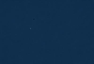 The primary subject of the image is the moon, which is visible in the sky. The setting is a clear blue sky, and the visual style is a photo. The colors and mood of the image are predominantly blue, creating a calm and serene atmosphere.