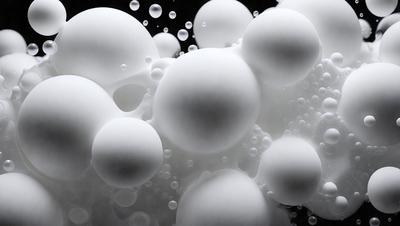 The primary subject of the image is a group of white, round, and bubbly objects, which are floating in a dark background. The setting appears to be a black background, which contrasts with the white bubbles. The visual style of the image is a close-up of the bubbles, showcasing their unique texture and appearance. The colors and mood of the image are predominantly dark and moody, with the white bubbles providing a contrasting and luminous element.