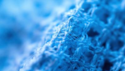The primary subject of the image is a close-up of a blue fabric with a fuzzy texture. The setting is a blue background, which creates a contrast with the fabric. The visual style is a close-up of the fabric, showcasing its texture and details. The colors in the image are predominantly blue, giving the scene a calm and soothing atmosphere.